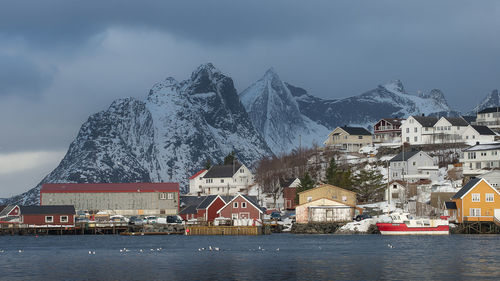 Buildings by lake against sky during winter