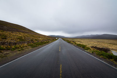 Empty road by mountain against cloudy sky