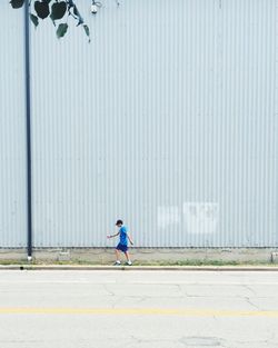 Man walking on sidewalk amidst road and wall