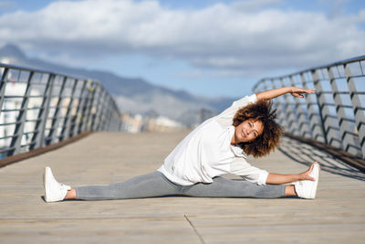 Full length of young woman exercising on bridge against sky