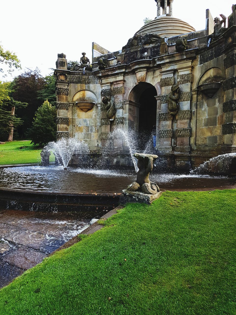 water, architecture, fountain, motion, built structure, splashing, building exterior, outdoors, waterfall, nature, grass, long exposure, spraying, day, history, real people, beauty in nature, sky, one person, people