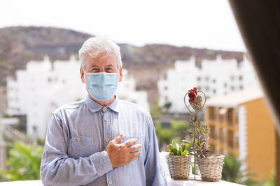 Portrait of senior man wearing mask gesturing against building