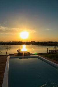 Swimming pool by lake against sky during sunset