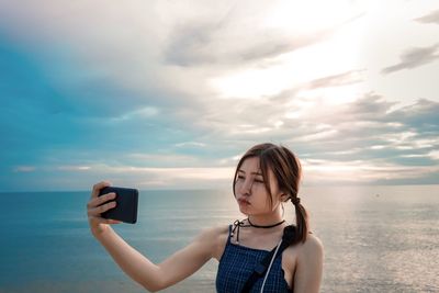 Young woman taking selfie while standing against sky