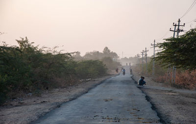 People riding bicycle on road against sky in city