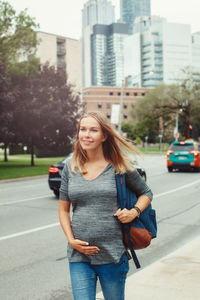 Pregnant woman walking sidewalk in city