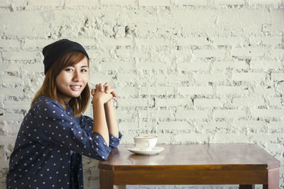 Portrait of young woman with coffee cup on table sitting in cafe