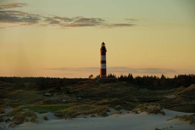 Lighthouse amidst buildings against sky during sunset