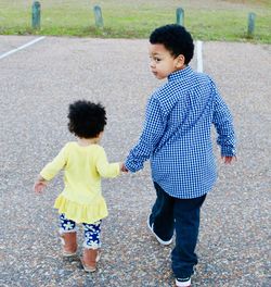 Rear view of siblings holding hands while walking on footpath