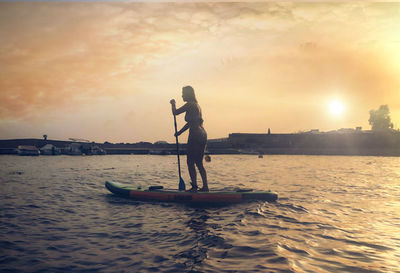 Rear view of man standing in boat on sea against sky during sunset