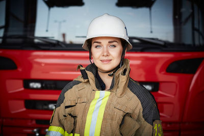 Portrait of female firefighter wearing helmet against fire engine at fire station