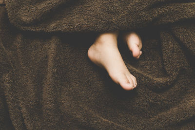 Low section of child with blanket relaxing on bed