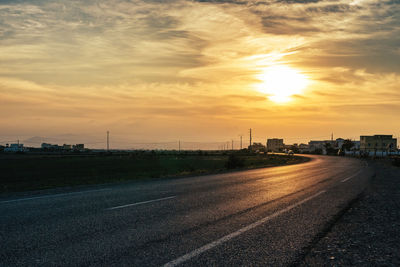 Road by city against sky during sunset