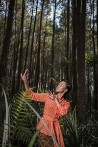 Woman standing by tree trunk in forest