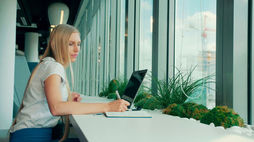 Side view of young woman using laptop at home