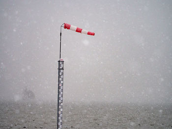 Windsock on pole in sea against sky during snowy weather