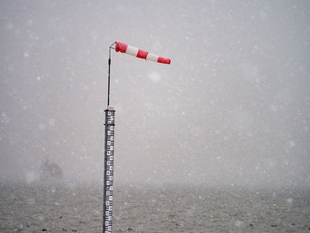 Red flag on pole by sea against sky