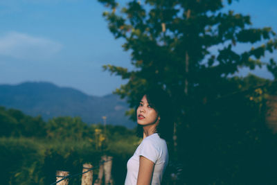 Side view of young woman standing against trees