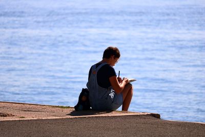 Man sitting on retaining wall by sea