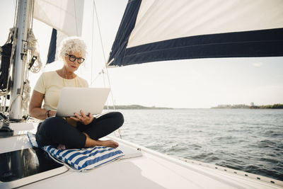 Senior woman working remotely while sailing boat on sunny day