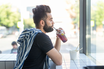 Side view of young man standing by window