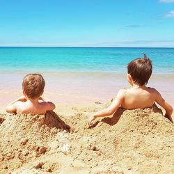 Rear view of shirtless boy at beach against sky