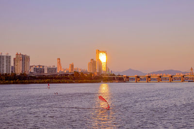 City at waterfront against sky during sunset