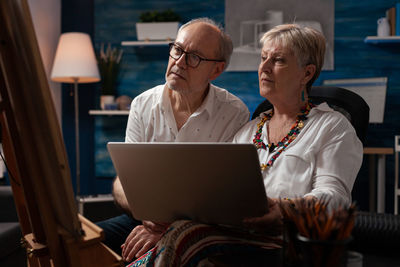 Senior couple with laptop looking at canvas