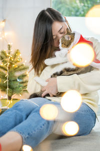 Woman embracing cat while sitting by christmas decoration