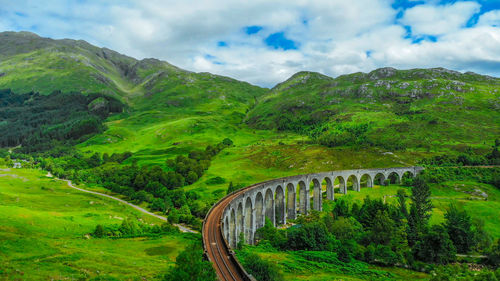 Arch bridge amidst trees and mountains against sky