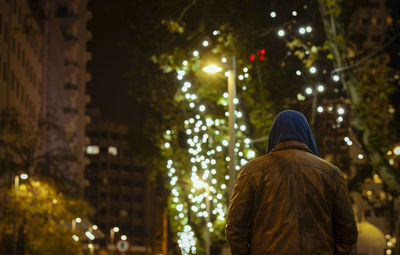 Rear view of woman standing by illuminated christmas tree at night
