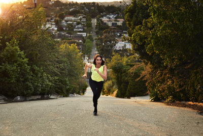 Full length of jogger running on road amidst trees during sunset