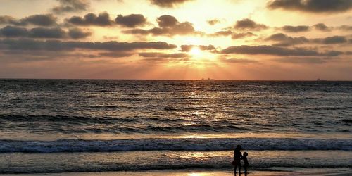 Children at beach against cloudy sky during sunset