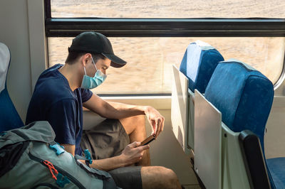 Backpacker with face mask using mobile phone while traveling by train.