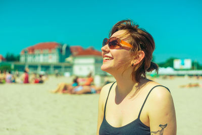 Smiling young woman wearing sunglasses at beach during sunny day