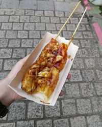 Cropped hand holding food at sidewalk