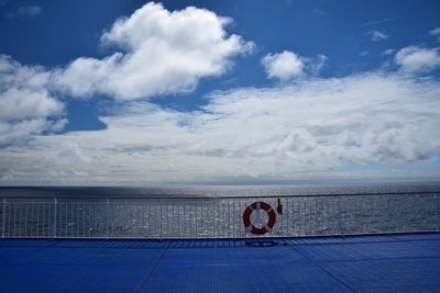 Lifebelt on railing of boat deck at sea against cloudy sky