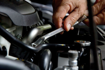 Cropped hand of mechanic repairing car engine with wrench