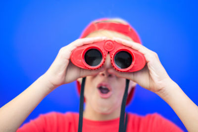 Close-up of boy looking through binoculars against blue background