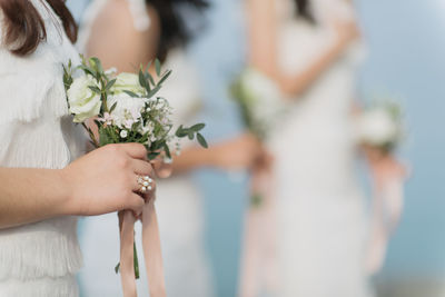 Midsection of bridesmaids holding bouquet while standing outdoors