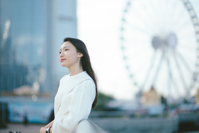 Young woman looking away while standing by railing in city