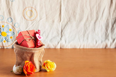 Close-up of artificial flowers and gift in sack on wooden table