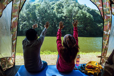 Rear view of people sitting on mat by lake