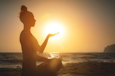 Side view. silhouette shot at sunset or sunrise. young caucasian woman meditating in the lotus