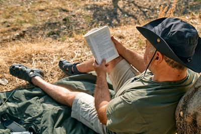 Bearded man tourist relaxing after hiking under the tree with book, reading novel in autumn park.