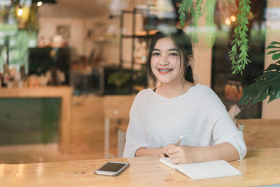 Portrait of smiling young woman using smart phone at table