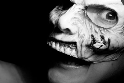 Close-up portrait of woman wearing spooky mask against black background