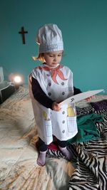Girl in chef costume holding paper while standing on bed
