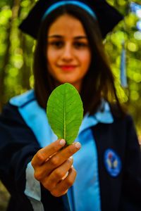 Portrait of young woman wearing graduation gown while holding leaf outdoors