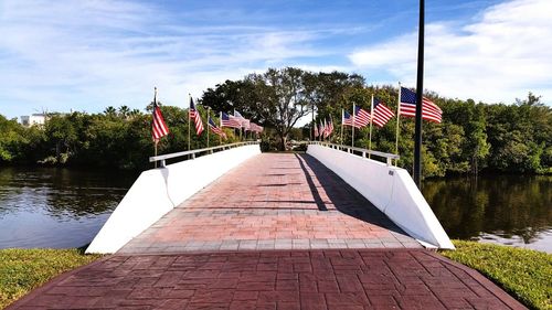 American flags on bridge over river against sky